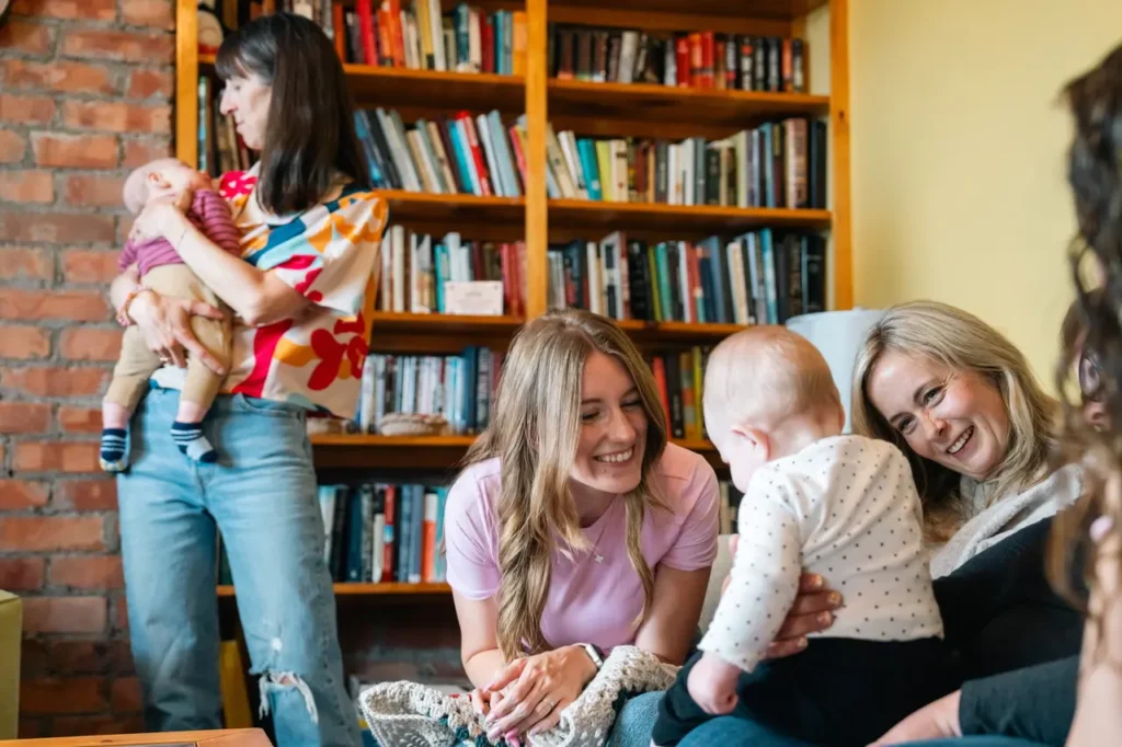 Close-up of parents interacting with their children in a bright room. One mother is standing and hugging her child, while two other parents are sitting on the couch, smiling at a happy child.